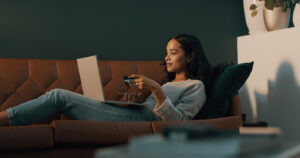 Shot of young woman using her credit card and laptop to shop online while relaxing at home.